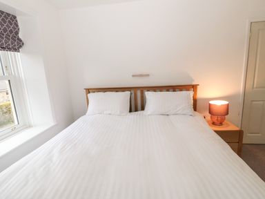 A bedroom with a double bed two pillows bedside table with lamp and window at Tyne View Cottage in Bellingham