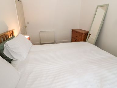 A bedroom with a bed a wooden chest of drawers a standing mirror a radiator and a closed door at Tyne View Cottage in Bellingham