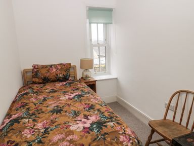 A small bedroom with a single bed with floral bedding a wooden chair a window and a bedside table with a lamp at Tyne View Cottage in Bellingham