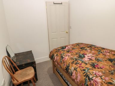A small bedroom with a bed with floral bedding a wooden chair and a wooden chest against a white wall at Tyne View Cottage in Bellingham
