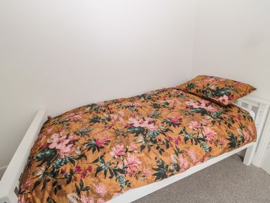 A single bed with floral bedding in a white-walled room at Tyne View Cottage in Bellingham