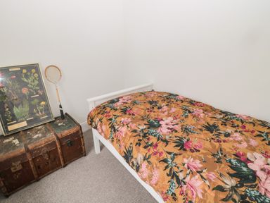 A small bedroom with a single bed with floral bedding and a vintage trunk with a badminton racket and a framed botanical print at Tyne View Cottage in Bellingham
