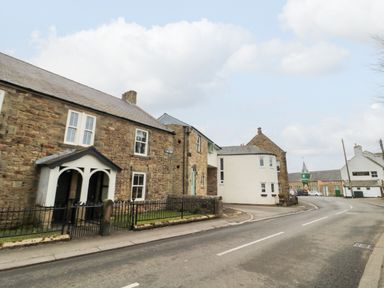A street with historic stone buildings and a clock tower in the background at Tyne View Cottage in Bellingham