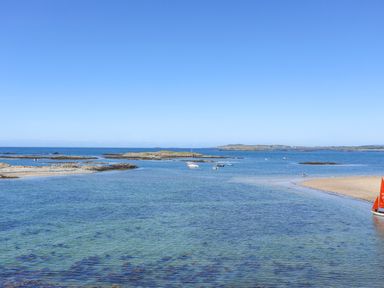 A coastal scene with clear water boats and rocky islands at Wingelock in Rhosneigr