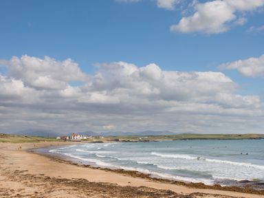 A sandy beach with waves and houses near the shore at Wingelock in Rhosneigr