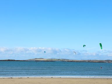 A beach with sand and ocean with kite surfers in the water at Wingelock in Rhosneigr