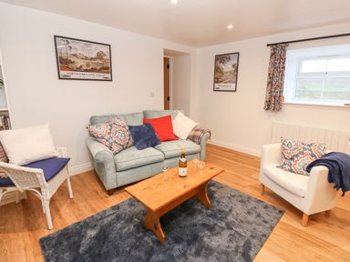 A living room with a sofa chairs wooden coffee table and framed pictures on wall at The Byre in Carrshield near Allendale