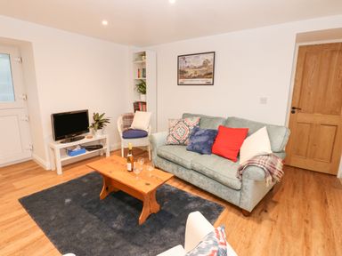 A living room with a sofa bed with several cushions a wooden coffee table with a bottle and glasses a small television on a white stand and a white armchair at The Byre in Carrshield near Allendale