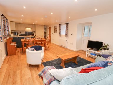 An open plan living and dining room with a sofa a coffee table a television dining table with chairs and a kitchen at The Byre in Carrshield near Allendale