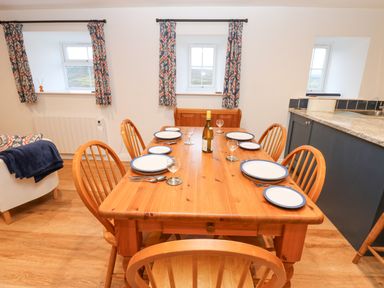 A wooden dining table set with plates glasses and cutlery in a room with windows and blue patterned curtains at The Byre in Carrshield near Allendale