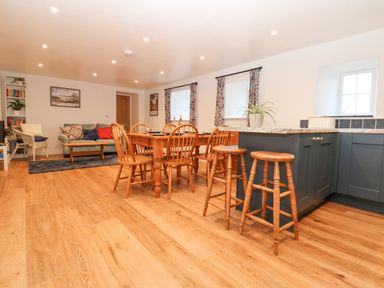 A living area with a wooden dining table and chairs a kitchen island with stools and a sitting area at The Byre in Carrshield near Allendale