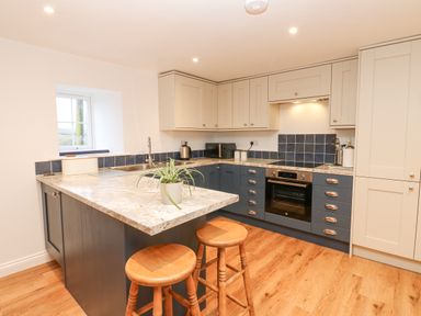 A kitchen with a countertop island and two wooden stools a sink oven cabinets and a small plant on the counter at The Byre in Carrshield near Allendale
