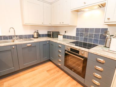 A kitchen with blue lower cabinets and white upper cabinets a sink an electric oven a microwave and kitchen utensils at The Byre in Carrshield near Allendale