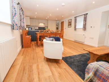 A dining area with wooden table and chairs next to a kitchen with cabinets and a white armchair on wooden floor at The Byre in Carrshield near Allendale