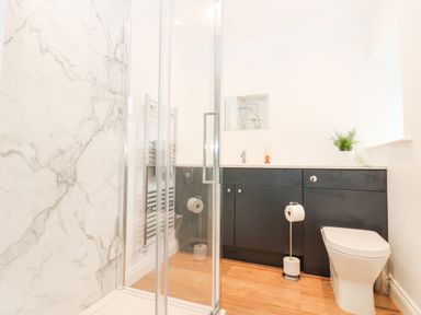 A bathroom with a glass shower enclosure black cabinets a white toilet and a towel radiator at The Byre in Carrshield near Allendale