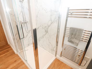 A shower enclosure with glass doors and marble-patterned walls next to a chrome towel radiator with a towel at The Byre in Carrshield near Allendale