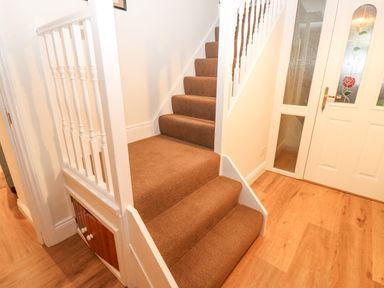 A staircase with brown carpet and white railing next to a white door with patterned glass panels at The Byre in Carrshield near Allendale