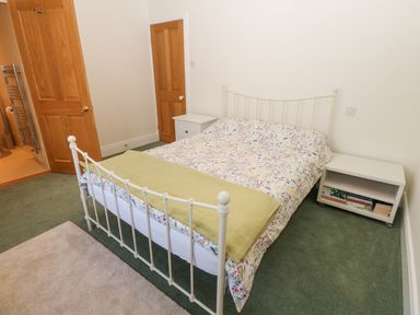 A bedroom with a double bed with floral bedding and two white bedside tables one with books at The Byre in Carrshield near Allendale