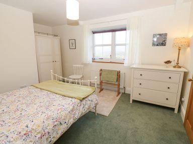 A bedroom with a bed a wardrobe a chair a window and a chest of drawers at The Byre in Carrshield near Allendale