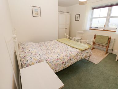 A bedroom with a floral bedspread on a metal bed frame a white wardrobe a chair and a towel rack by the window at The Byre in Carrshield near Allendale