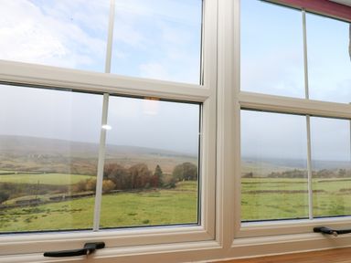 A view of green fields hills and trees through a window at The Byre in Carrshield near Allendale