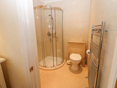 A bathroom with a glass shower enclosure a toilet a heated towel rail and a wooden vanity unit with storage at The Byre in Carrshield near Allendale