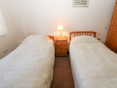 A bedroom with two single beds a wooden nightstand and a lamp at The Byre in Carrshield near Allendale