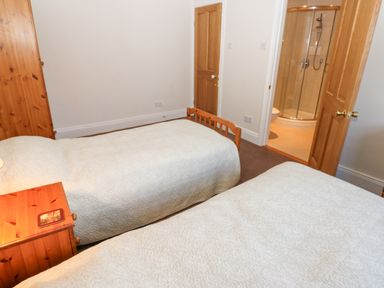 A bedroom with two single beds a wooden nightstand and an en suite bathroom at The Byre in Carrshield near Allendale