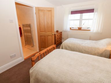 A bedroom with two single beds a wooden dresser a window with curtains and an open door leading to a bathroom at The Byre in Carrshield near Allendale