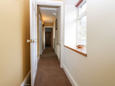 A narrow hallway with a window ledge holding a bowl and a partially open white door at The Byre in Carrshield near Allendale