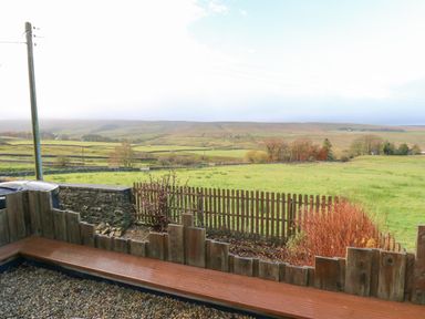 A wooden bench and wooden fence overlooking green fields and hills at The Byre in Carrshield near Allendale
