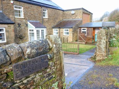 Stone house with multiple windows and a small garden behind a stone wall with a wooden sign Southview Carrshield near Allendale