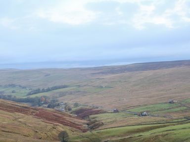 A wide landscape view of rolling hills with scattered buildings and fields separated by stone walls at The Byre in Carrshield near Allendale