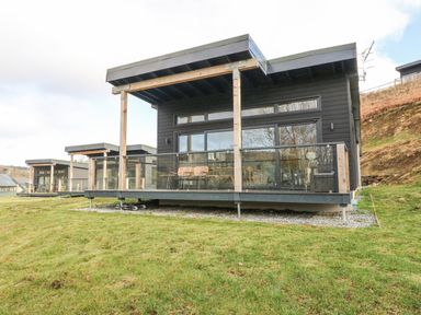 A row of modern cabins with glass balconies on a grassy hillside at Coorie In in Aberfeldy