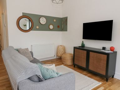 A living room with a gray sofa a wall-mounted television and a cabinet at Coorie In Aberfeldy