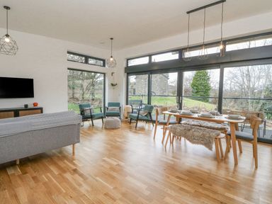 A living room and dining area with wooden floor large windows and green chairs at Coorie In Aberfeldy
