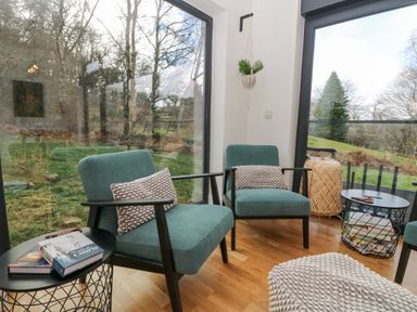 A seating area with two chairs and round tables by large windows overlooking a garden at Coorie In in Aberfeldy