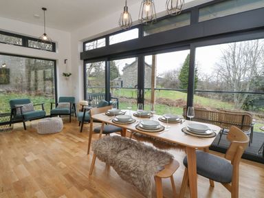 A dining room with a wooden table set for six and seating including chairs and a bench with fur at Coorie In Aberfeldy