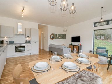 A kitchen and living area with a dining table set for six and large windows at Coorie In in Aberfeldy