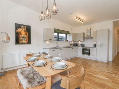 A kitchen and dining area with a wooden table set for six and modern cabinets at Coorie In Aberfeldy