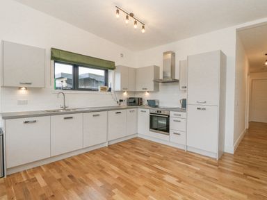 A modern kitchen with white cabinets wooden floor and appliances at Coorie In Aberfeldy