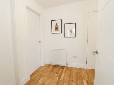 A hallway with three white doors two framed pictures on the wall and a radiator on a wooden floor at Coorie In Aberfeldy