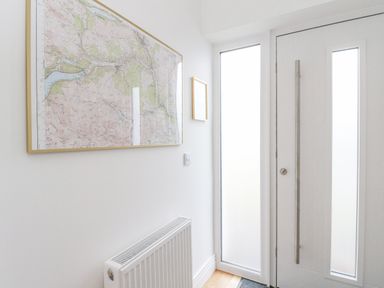 A hallway with a white door featuring vertical glass panels a radiator beneath a large framed map and a small framed picture at Coorie In Aberfeldy