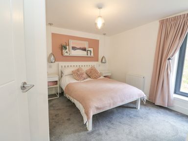 A bedroom with a double bed pink blankets and pillows bedside tables and lamps and a window with pink curtains at Coorie In Aberfeldy