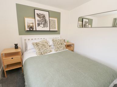 A bedroom with a bed with green bedding and two wooden bedside tables with lamps at Coorie In Aberfeldy