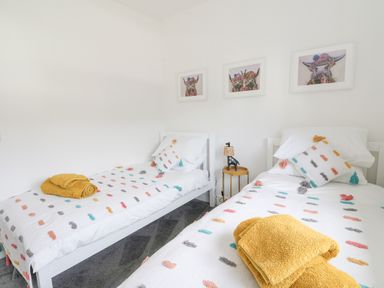 A bedroom with two single beds white bed frames and colorful blankets with art above the beds at Coorie In in Aberfeldy