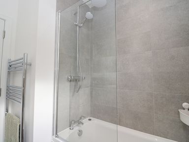 A bathroom with a bathtub shower and towel rack at Coorie In Aberfeldy