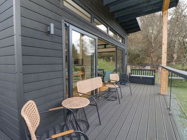An outdoor deck with woven chairs a bench and glass railing at Coorie In in Aberfeldy