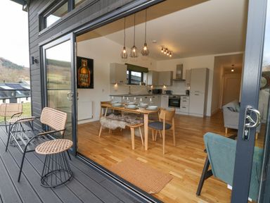 A kitchen and dining area with a wooden table set for six and a seating area with chairs at Coorie In Aberfeldy