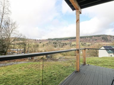 A view from a balcony with glass railing overlooking a grassy field and hills at Coorie In in Aberfeldy